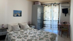 Une chambre à coucher comprenant un lit, une table de chevet, un bureau avec une chaise, une armoire et un téléviseur.
