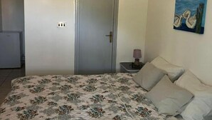 Une chambre à coucher avec un lit, une porte, une table de chevet avec une lampe et un tableau au mur.