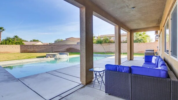 Un patio techado con piscina, mobiliario exterior y vista a casas vecinas.
