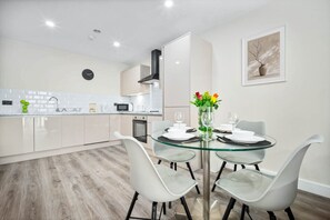 Cozinha moderna com armários brancos, uma mesa de jantar de vidro e um vaso com flores.