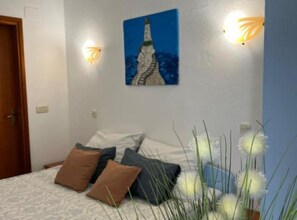 Un dormitorio con cama, almohadas, un cuadro y apliques de pared.