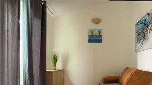 Una habitació amb un sofà marró, una petita taula auxiliar de fusta amb una planta, una prestatgeria penjada a la paret i un quadre.
