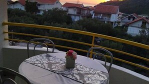 A balcony with a table and chairs, overlooking a residential area with houses and a mountain in the background. - Apartments Natali - One Bedroom Apartment with Balcony (APP5) (Podaca)