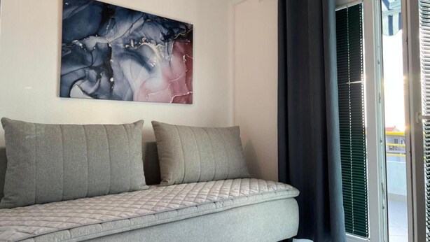 Un salon moderne avec un canapé gris, un grand tableau abstrait et une porte-fenêtre coulissante avec des stores verts.