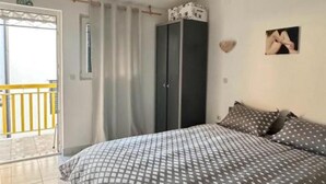 Une chambre à coucher comprenant un lit, une armoire, une porte donnant sur un balcon extérieur et un tableau accroché au mur.