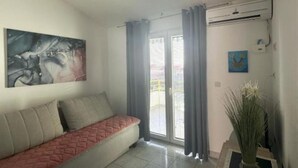 Un salon avec un canapé, un tableau, une plante en pot et une porte-fenêtre coulissante.