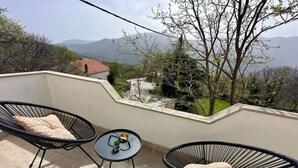 A balcony with two black wire-framed chairs, a small round table with a bowl and a plant, and a view of a mountainous landscape. - Two Bedroom Apartment with Terrace and Swimming pool (Zagvozd)