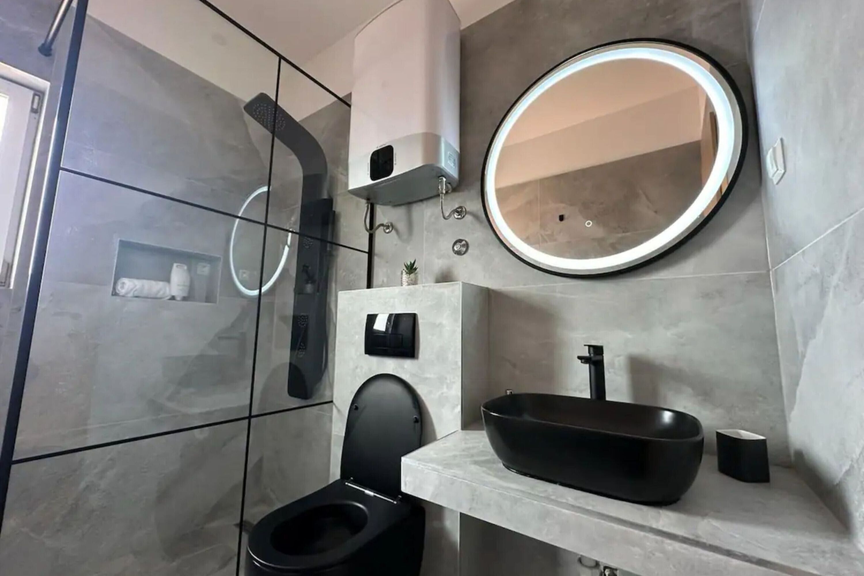 Une salle de bain moderne avec des toilettes noires, un miroir rond, un lavabo noir et un lave-linge encastré.