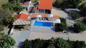 En vy från ovan av en fastighet med en swimmingpool, utomhusmöbler och en byggnad med rött tak.