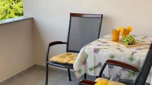 Ein Balkon mit zwei Korbstühlen, einem Tisch mit blumigem Tischtuch und einer kleinen Obstschale.
