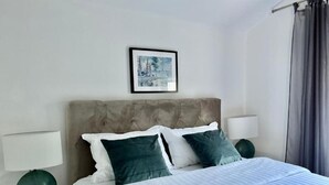 Ein ordentlich eingerichtetes Schlafzimmer mit einer gepolsterten Kopfteile, einem gerahmten Bild an der Wand und einem Bett mit weißer und dunkelgrüner Bettwäsche.