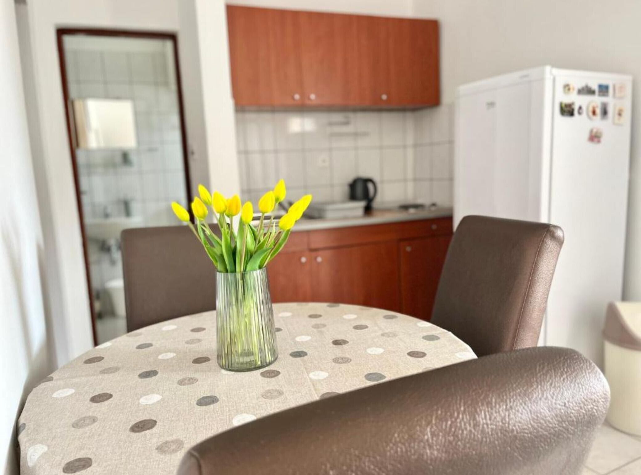 Una mesa de comedor con mantel de lunares, un jarrón con flores amarillas y una silla de cuero marrón.