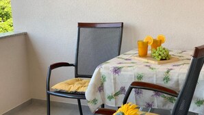 Ein Balkon mit zwei Stühlen, einem Tisch mit einer blumigen Tischdecke und einer Schale mit Trauben und einem Glas Orangensaft.