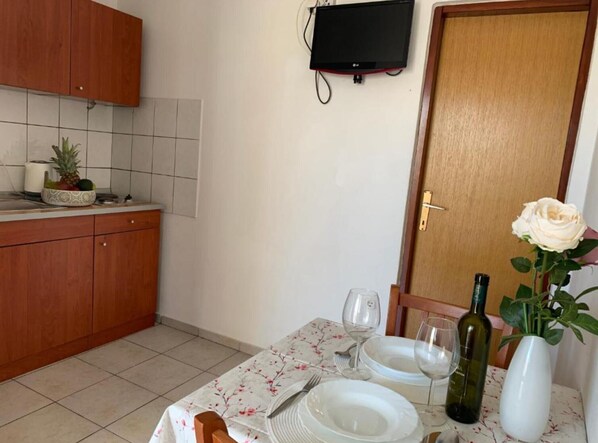 Une cuisine avec des meubles en bois, un plan de travail recouvert de carreaux, un panier de fruits et un coin repas avec une table mise pour deux personnes.