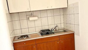 A small kitchen with wooden cabinets, a stainless steel sink, and a tiled backsplash. - Apartments Fortuna - Studio Apartment (Biograd na Moru)