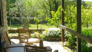 Un patio con sillas y una mesa de madera, rodeado por un jardín con diversas plantas y flores.