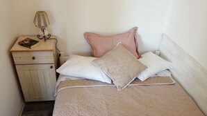 Una cama bien hecha con un colcha color beige, una mesita de noche de madera con una lámpara y un libro.