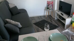 Una sala de estar con un sofá gris, una mesita con un vaso y un televisor sobre un mueble.