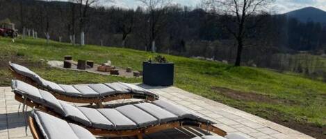 Outdoor sun loungers with a view of a forest and mountains.