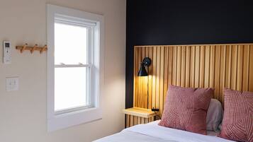 A bedroom with a bed, a bedside table, a lamp, a window, and a wall-mounted light fixture.