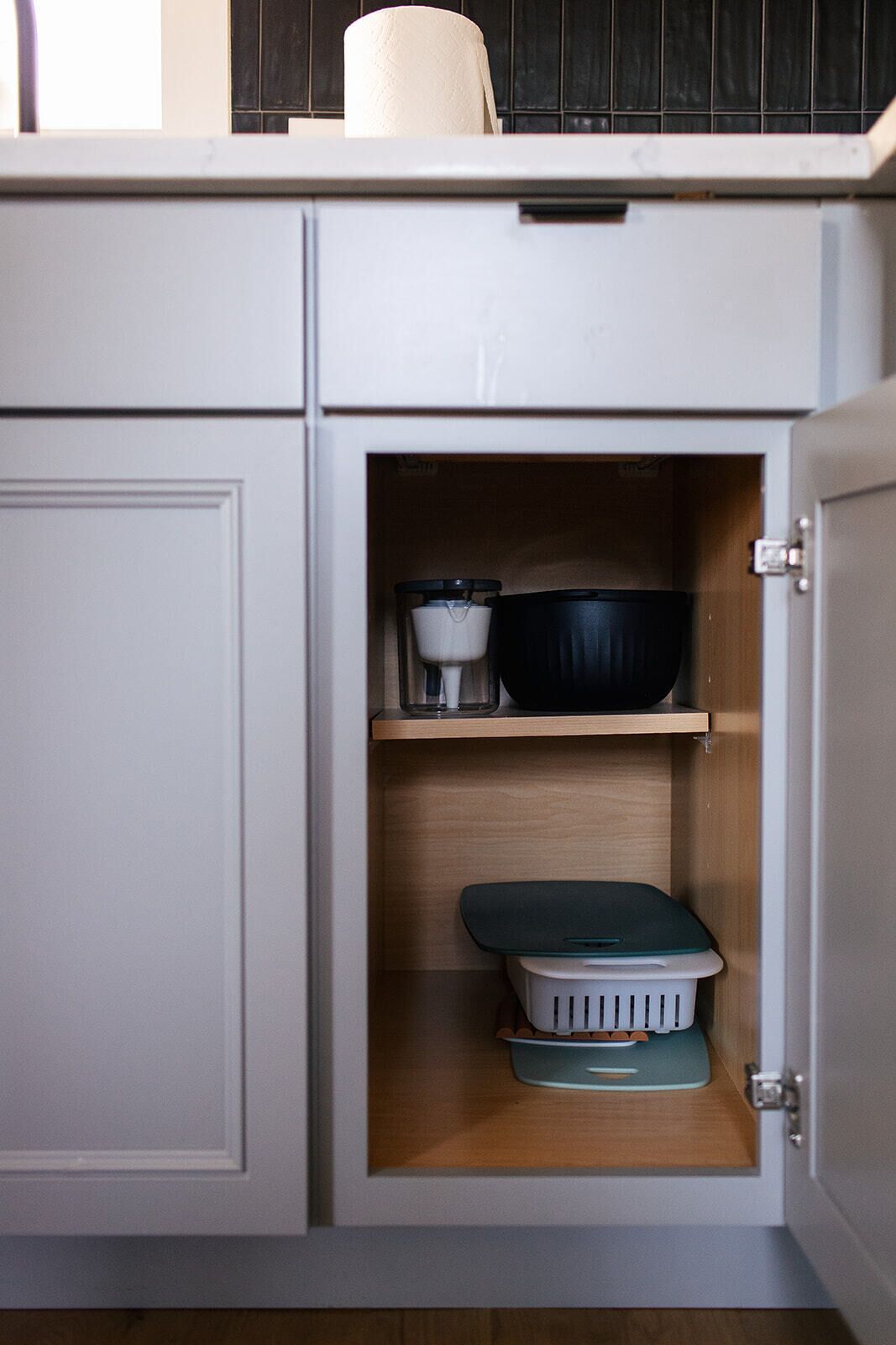 A kitchen cabinet with a microwave, a black pot, a white container, and a green tray.