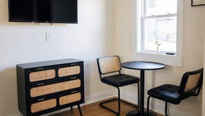 A room with a flat-screen TV mounted on the wall, a black entertainment unit with wicker panels, two black chairs with wicker backs, and a small round table. - The Mane & Co - No. 4 (Chambersburg)