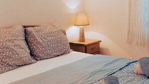 A neatly made bed with floral-patterned pillows and a blue bedspread, a bedside lamp, and a framed picture on the wall. - Hvar spa & apartments-1 Bedroom-Terrace/Sea View 3 (Vrboska)