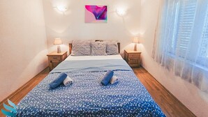 A bedroom with a bed, two bedside tables, a wall-mounted artwork, and a window with curtains. - Hvar spa & apartment-2 Bedroom-Terrace/Sea View 4 (Vrboska)