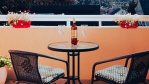 Eine Terrasse mit zwei Stühlen und einem Tisch, einer Weinflasche und zwei Gläsern auf dem Tisch.