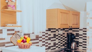 Eine kleine Küche mit Holzausbau, einem weißen Kühlschrank, einer Kaffeemaschine und einer Obstschale auf der Arbeitsplatte.