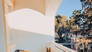 A small balcony with a round table, two chairs, a potted plant, and a view of a residential area with trees and houses. - One Bedroom Apartment with Bacony and Sea View (Vrboska)