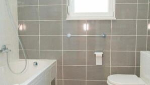 Une salle de bain avec une baignoire, des toilettes et une fenêtre.