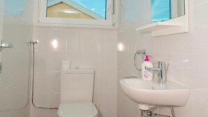 Une salle de bain avec des toilettes, un lavabo et une fenêtre située au-dessus des toilettes.