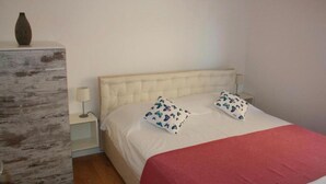 Une chambre à coucher avec un lit, deux oreillers, une table de chevet, une lampe et un vase posé sur une commode.