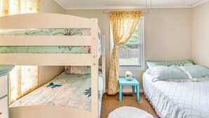 Een slaapkamer met een stapelbed, een plafondventilator, een raam met gordijnen en een tafeltje met zakdoekjes.