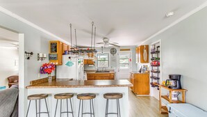 Een moderne keuken met een centraal eiland, een paar barkrukken, houten kastjes en een plafondventilator.