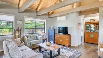 A spacious living room with a high ceiling, large windows, a wooden entertainment center, and a cozy seating area.