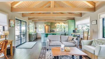 A spacious living area with a wooden ceiling, a sofa, a coffee table, and a view of the kitchen.