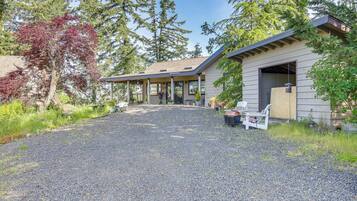 A gravel driveway leading to a wooden cabin with a covered porch, surrounded by trees and greenery.