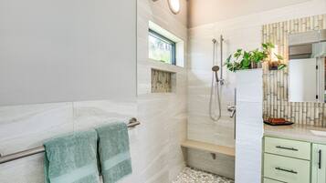A modern bathroom with a shower, a window, and a green towel rack.