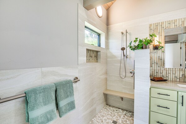 A modern bathroom with a shower, a window, and a green towel rack.