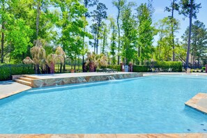 Une piscine bordée de pierres, entourée d’arbres et d’une clôture.