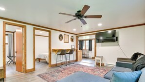 A modern living room with a blue sofa, a ceiling fan, and a kitchen area in the background.