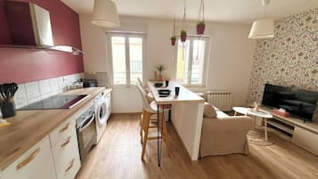 A modern kitchen with a central island, a dining area, and a living space with a TV.