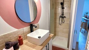 Une salle de bain moderne avec un grand miroir rond, un lavabo blanc et une douche à parois de verre.