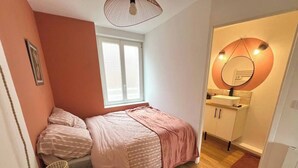 Une petite chambre à coucher avec un lit, une fenêtre, un miroir et un lavabo dans la salle de bain.