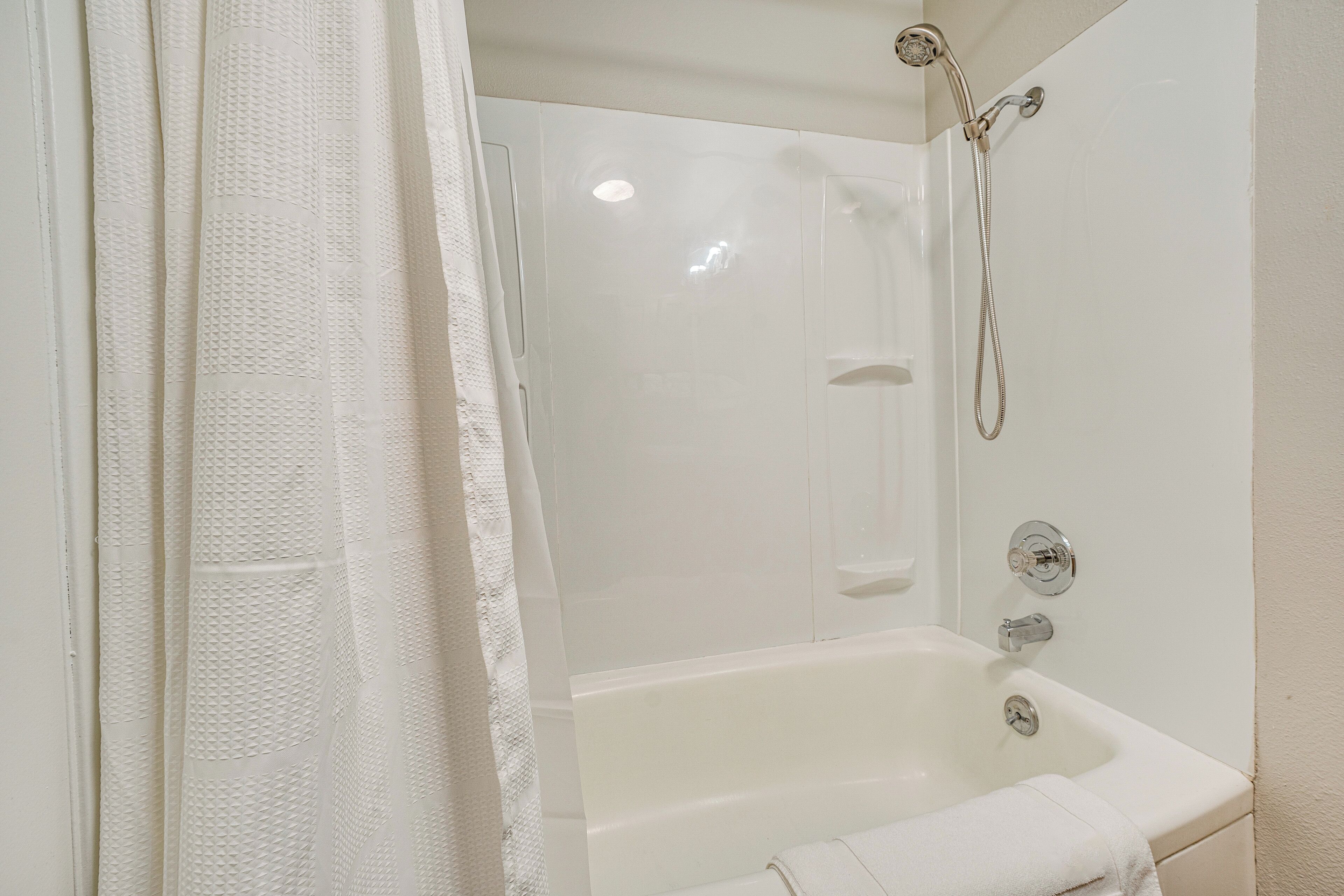 A white bathroom with a bathtub, shower, and a towel on the floor.