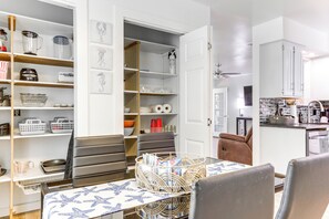 Een eetgedeelte met een tafel voor twee personen, een keuken op de achtergrond en een voorraadkast met gevulde planken.