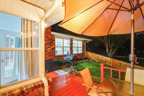 Een overdekt terras met een barbecue, tuinmeubels en uitzicht op de achtertuin.