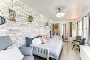 Een slaapkamer met een witte bakstenen muur, een bed met blauw beddengoed, een grijze bank en een stoel.